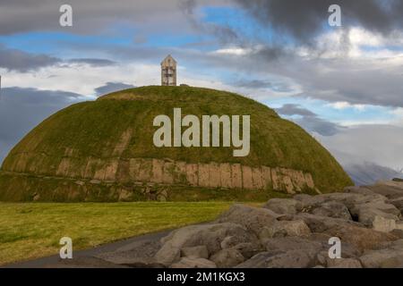 Thufa Hill come luogo di meditazione e serenità, basato sul folclore locale. Coperto da erba verde. Cielo nuvoloso piovoso. Grandi, porto di Reykjavik, Icel Foto Stock