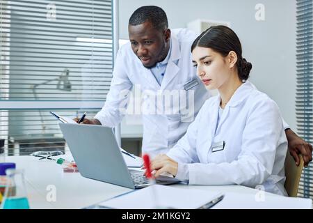 Ritratto di giovane donna che usa il portatile in laboratorio medico con capo scienziato Foto Stock