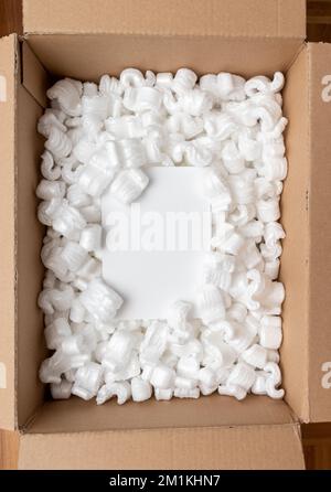 Una scatola di cartone riempita con pellet di schiuma di styro e spazio per la copia di cartoncini bianchi. Concetto di imballaggio o ordine di acquisto online. Foto Stock
