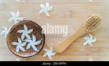 Spazzola massaggiante su sfondo in legno con fiori, salone termale, cura personale Foto Stock