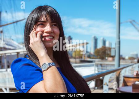 felice giovane donna caucasica latina di etnia venezuelana, sorridente parlando al telefono, seduto fuori di un ristorante, in attesa del cameriere, copia sp Foto Stock