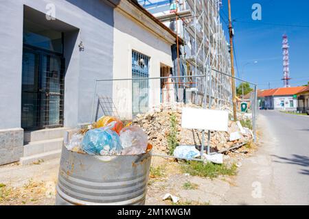 Cestino realizzato localmente, un fusto di metallo tagliato di fronte alla recinzione del cantiere accanto alla strada Foto Stock