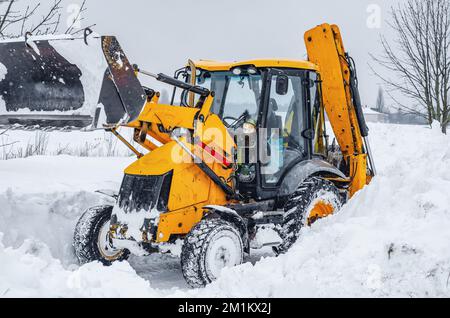 Il grande trattore giallo pulisce la neve dalla strada. Pulizia e pulizia delle strade della città dalla neve in inverno Foto Stock