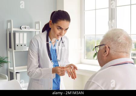 La giovane donna medico parla di benefici e prescrive l'assistenza all'udito per l'uomo anziano in clinica. Foto Stock