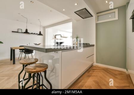 una cucina moderna con pavimento in legno e armadietti bianchi in camera è illuminata da lampade incassate sul soffitto Foto Stock