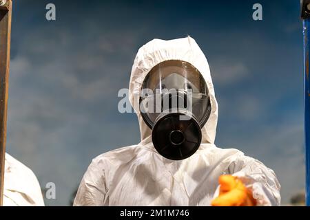 Ritratto del tecnico industriale che indossa tuta in zerbino in stabilimento di produzione. Uomo in uniforme protettiva bianca con maschera di protezione che maneggia haza Foto Stock