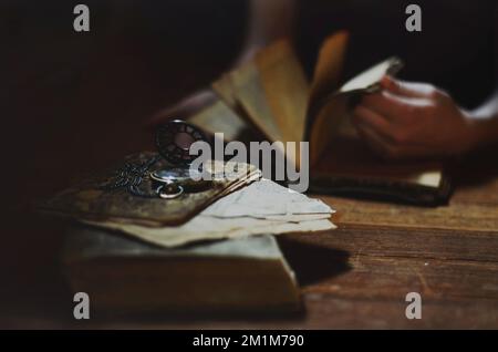 Le mani scorrono tra pile di vecchi libri e un orologio tascabile Foto Stock