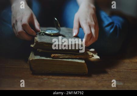 Le mani scorrono tra pile di vecchi libri e un orologio tascabile Foto Stock