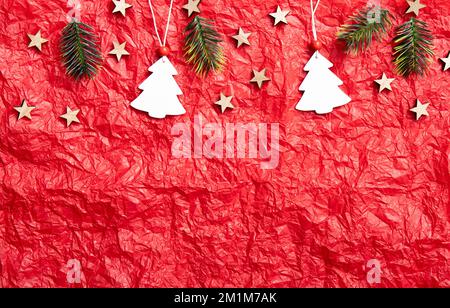 Sfondo rosso crumpled di carta di seta con decorazioni natalizie sulla sezione superiore, molto spazio copia. Foto da studio. Ornamenti bianchi a forma di albero di Natale. Foto Stock