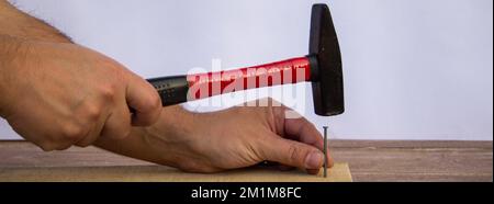 Immagine delle mani di un manipolo che tiene un chiodo con un martello mentre inchioda le tavole di legno. Lavori fai da te. Banner orizzontale Foto Stock