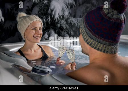coppia che si rilassa nella vasca idromassaggio all'aperto e beve champagne in inverno. fuga romantica, vacanza di luna di miele Foto Stock