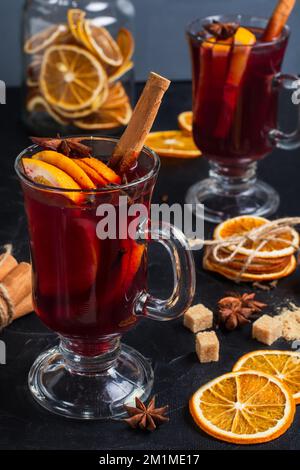 Due tazze di VIN brulé sulla tavola, vicino ad essa ci sono cannella, agrumi, arance secche, anice stellato, zucchero di canna. Produzione di VIN brulé a casa Foto Stock