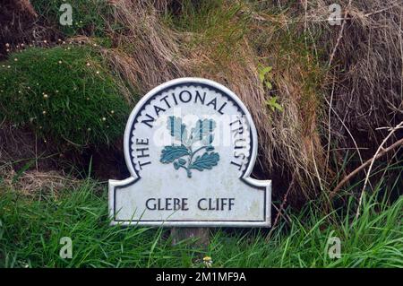 Metal National Trust Sign su un palo di legno per Glebe Cliff vicino a Tintagel dal South West Coastal Path in Cornovaglia, Inghilterra, Regno Unito. Foto Stock