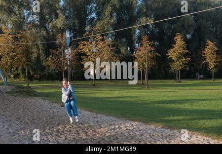 Divertimento autunnale all'aperto. Giovane ragazza in sella a un bungee appeso sul parco giochi Foto Stock