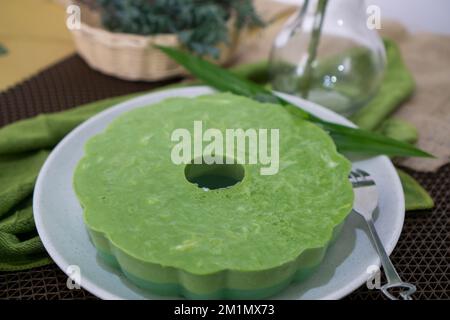 Cibo indonesiano, Puding Pandan Lumut in una ciotola bianca decorata con foglie di pandan e una forchetta con un motivo a cuore Foto Stock