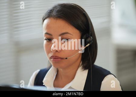 Primo piano ritratto di una giovane donna nera che indossa la cuffia e guarda lo schermo del computer nell'ufficio di assistenza clienti Foto Stock