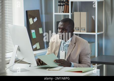 Ritratto di un uomo d'affari nero che utilizza un computer desktop in ufficio e che lavora con i documenti Foto Stock