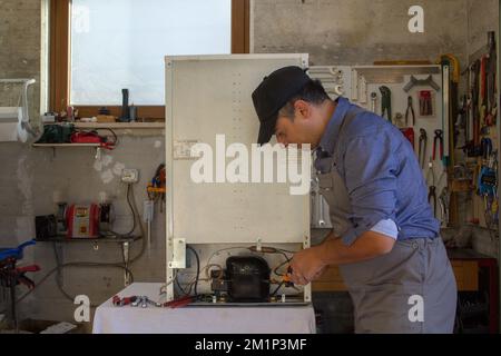 Tecnico dell'assistenza di apparecchi nella sua officina che ripara un frigorifero difettoso. Tecnico al lavoro in officina. Foto Stock