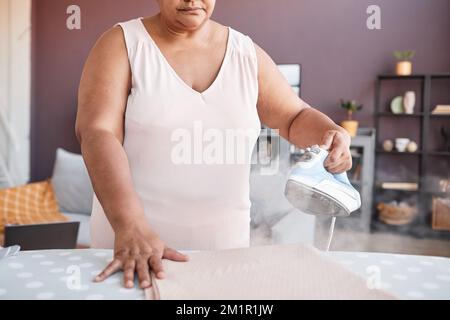 Primo piano dei vestiti neri anziani della donna che stira nella casa accogliente, fuoco sul vapore, spazio della copia Foto Stock