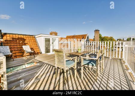 una terrazza con sedie, tavolo e ombrelloni all'ultimo piano di fronte ad un edificio di appartamenti con cielo blu Foto Stock