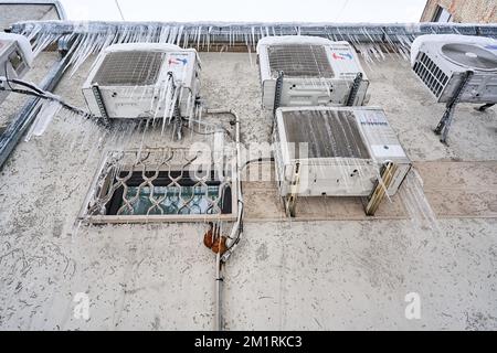 Riga, Lettonia - 12 dicembre, 2022: I condizionatori d'aria di varie marche montati sulla parete sono congelati e coperti da ghiaccio. Vista dal basso. Foto Stock