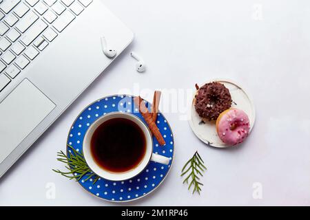 Stile di vita moderno con computer portatile, auricolari wireless, tazza da caffè, bastoncini di cannella con ciambelle. Webinar, freelance, lavoro online, ascolto di musica Foto Stock