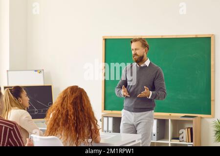 Ritratto di buon professore maschile durante la lezione con lavagna in gesso sullo sfondo. Foto Stock