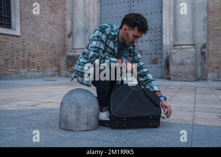 Musicista maschio aprendo la valigia per strada per iniziare a suonare il suo corno. Foto Stock