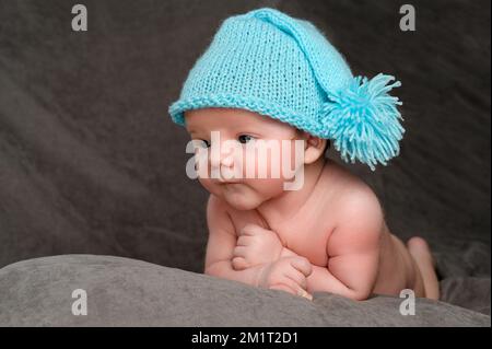 Rivne, Ucraina 25 aprile 2022: Un bambino neonato con un cappuccio blu giace sullo stomaco. Foto Stock