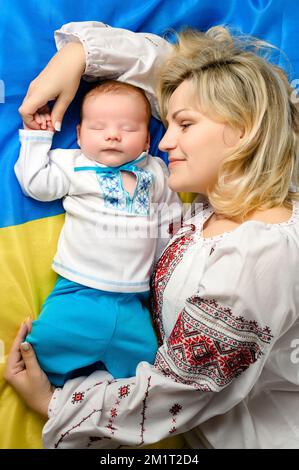 Rivne, Ucraina 25 aprile 2022: Un neonato vestito nazionale si trova e dorme sulla bandiera dell'Ucraina. Foto Stock