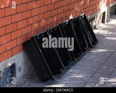 Cinque casse vuote di plastica nera per frutta e verdura appoggiate contro una parete di mattoni all'aperto Foto Stock