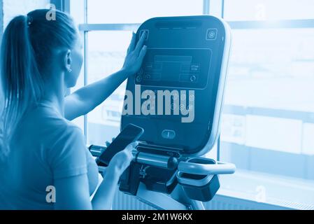 La donna le impostazioni di regolazione sulla macchina per allenamento in palestra Foto Stock