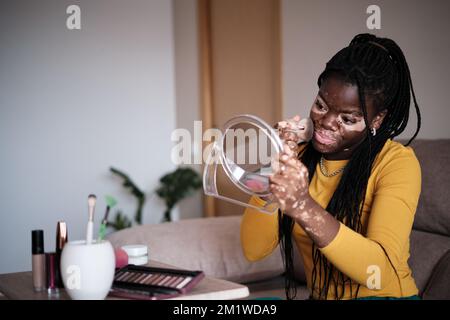 Donna nera positiva che applica il trucco a casa Foto Stock