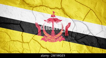 Bandiera di Brunei. Simbolo del Bruneian. Bandiera sullo sfondo di terra secca spaccata. Bandiera del Brunei con concetto di siccità Foto Stock
