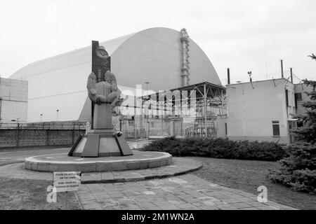 Monumento dei liquidatori di Chernobyl di fronte al grande contenitore a cupola del reattore 4th nel sito di esplosione della centrale nucleare di chernobyl. fotografia in bianco e nero Foto Stock