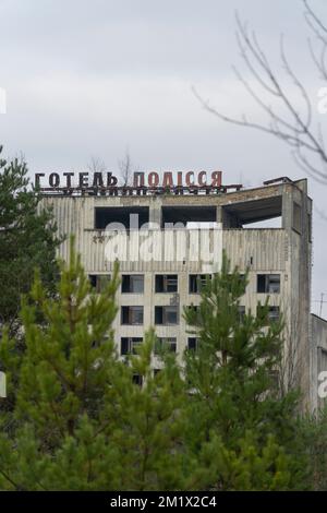 Cartello con la scritta Polissya Hotel in cima ad un edificio abbandonato con alto albero verde Foto Stock