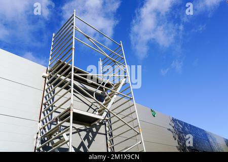 Moderna impalcatura in metallo accanto ad un nuovo edificio con facciata grigia a pannelli sandwich, sfondo blu cielo Foto Stock