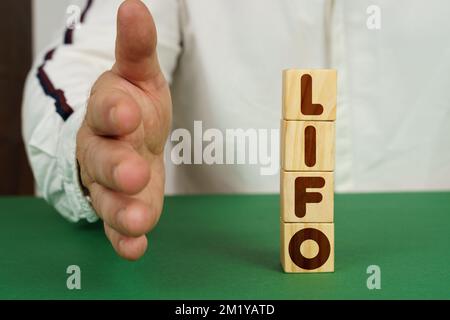 Concetto aziendale. Su una superficie verde, cubetti con l'iscrizione - LIFO. L'uomo tiene la mano. Foto Stock