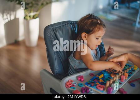 Bambina che fa attività per lo sviluppo motorio e sensoriale. Mani del bambino con giocattoli di legno colorati sul tavolo. Istruzione precoce. Foto Stock