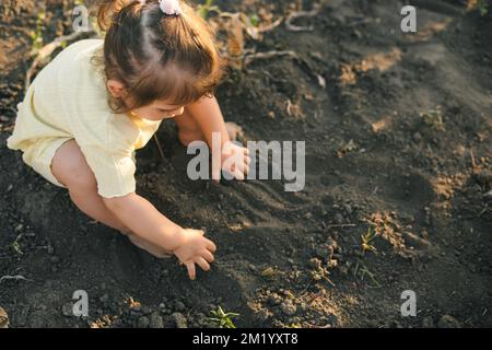 Ritratto di una bambina che preme il terreno con le mani. Divertimento per le vacanze estive. Concetto di agricoltura. Concetto di felicità. Foto Stock