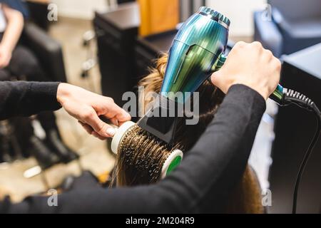 Master donna parrucchiere asciuga i capelli della ragazza con un asciugacapelli e pettini dopo il lavaggio nel salone di bellezza. Foto Stock