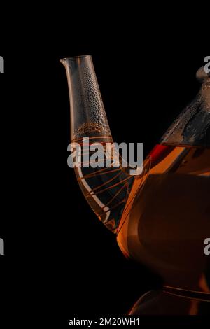 Beccuccio di bella teiera in vetro trasparente con tè close-up isolato su sfondo nero Foto Stock