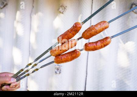 Salsicce alla griglia bavaresi, salsicce calde su spiedino. Barbecue all'aperto in mano Foto Stock