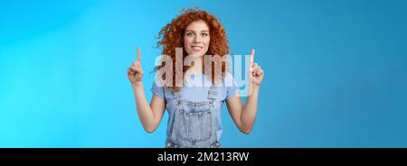 Motivata allegra redhead sciocca ricci donna che punta su inrdex dito sorridente affascinato impressionato eccitato mostrando impressionante promo discutere Foto Stock