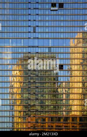 Vista astratta dei moderni edifici di uffici che si riflette nelle finestre di un altro moderno edificio di uffici. I pulitori per vetri funzionano su una piattaforma Foto Stock