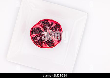 Shot di un mezzo melograno su un piatto bianco ritagliato in studio in vista dall'alto Foto Stock