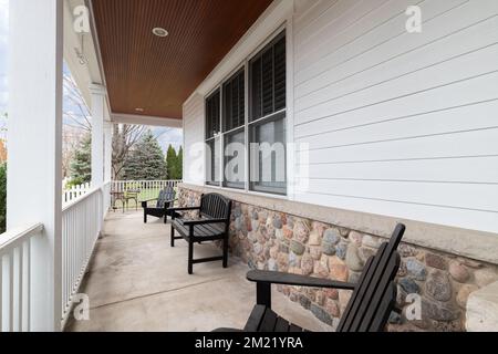 Il veranda avvolgente di una casa di lusso con rivestimento bianco e roccia e una recinzione bianca. Foto Stock