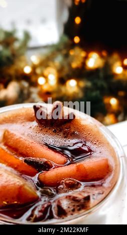 VIN brulé di Natale su sfondo sfocato di luci luminose. Tradizionale bevanda calda di Capodanno a base di vino rosso, arancia, cannella, mele e spezie di anice stellato. Cocktail X-mas. Messa a fuoco selettiva Foto Stock