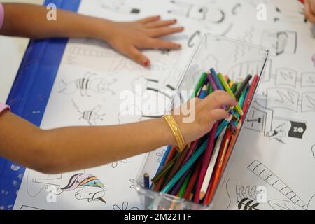 Un bambino siede e colora un gigantesco motivo di carta da colorare. Il bambino tiene in mano una matita. Un set di matite colorate su una scatola. Attività di disegno. Foto Stock