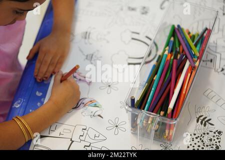 Un bambino siede e colora un gigantesco motivo di carta da colorare. Il bambino tiene in mano una matita. Un set di matite colorate su una scatola. Attività di disegno. Foto Stock